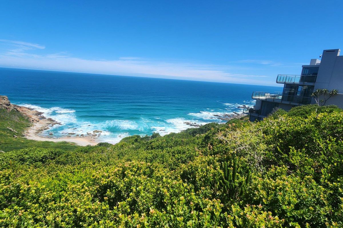 A scenic elevated view overlooking the coastline, featuring lush coastal vegetation and a modern multi-level residential property in the distance.