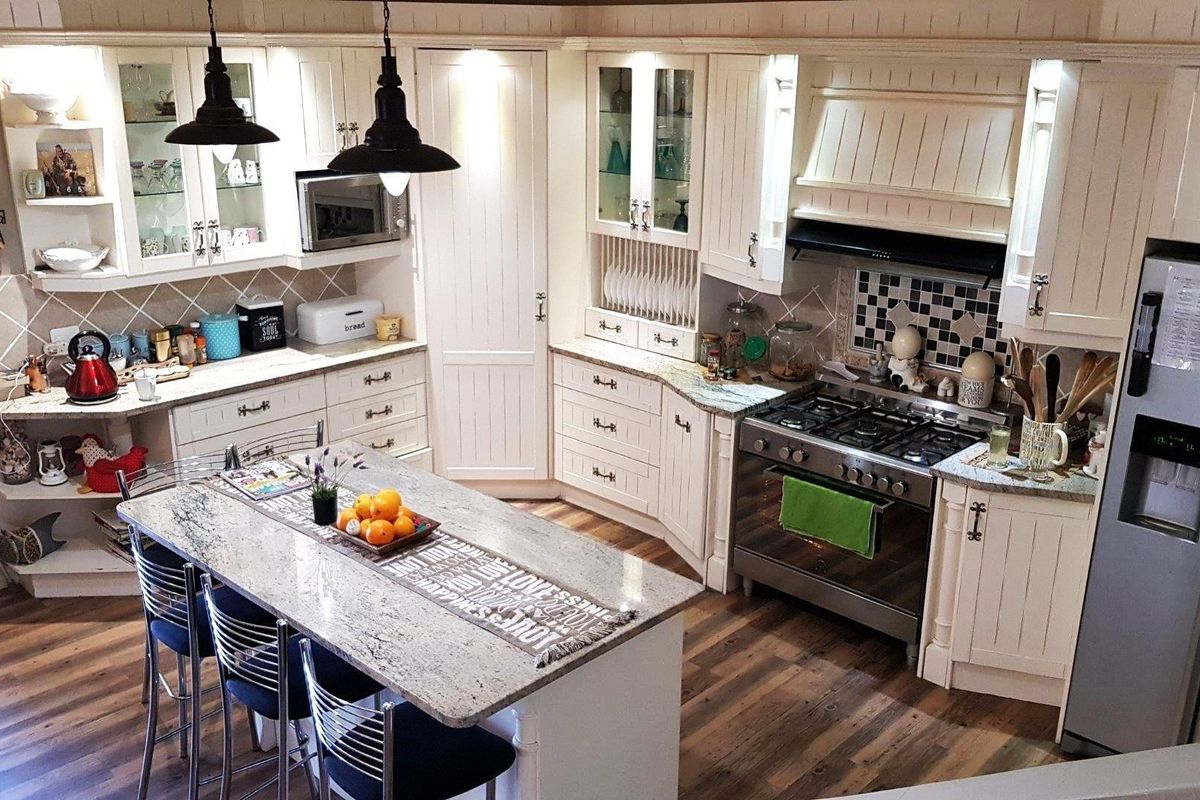 A well-appointed kitchen featuring cream cabinetry, granite countertops, a central island, and a gas range with a tiled backsplash.