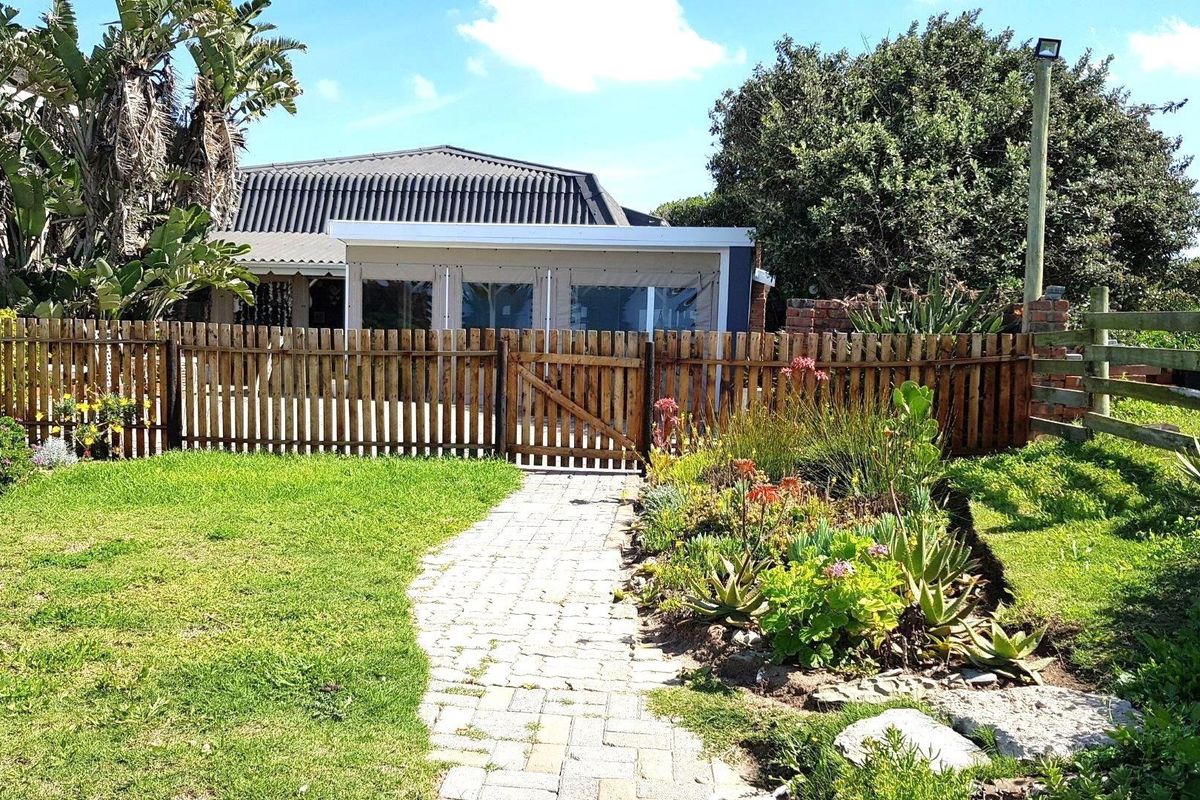 A well-maintained rear garden featuring a paved walkway leading to a wooden gate, picket fencing, and a covered patio area.
