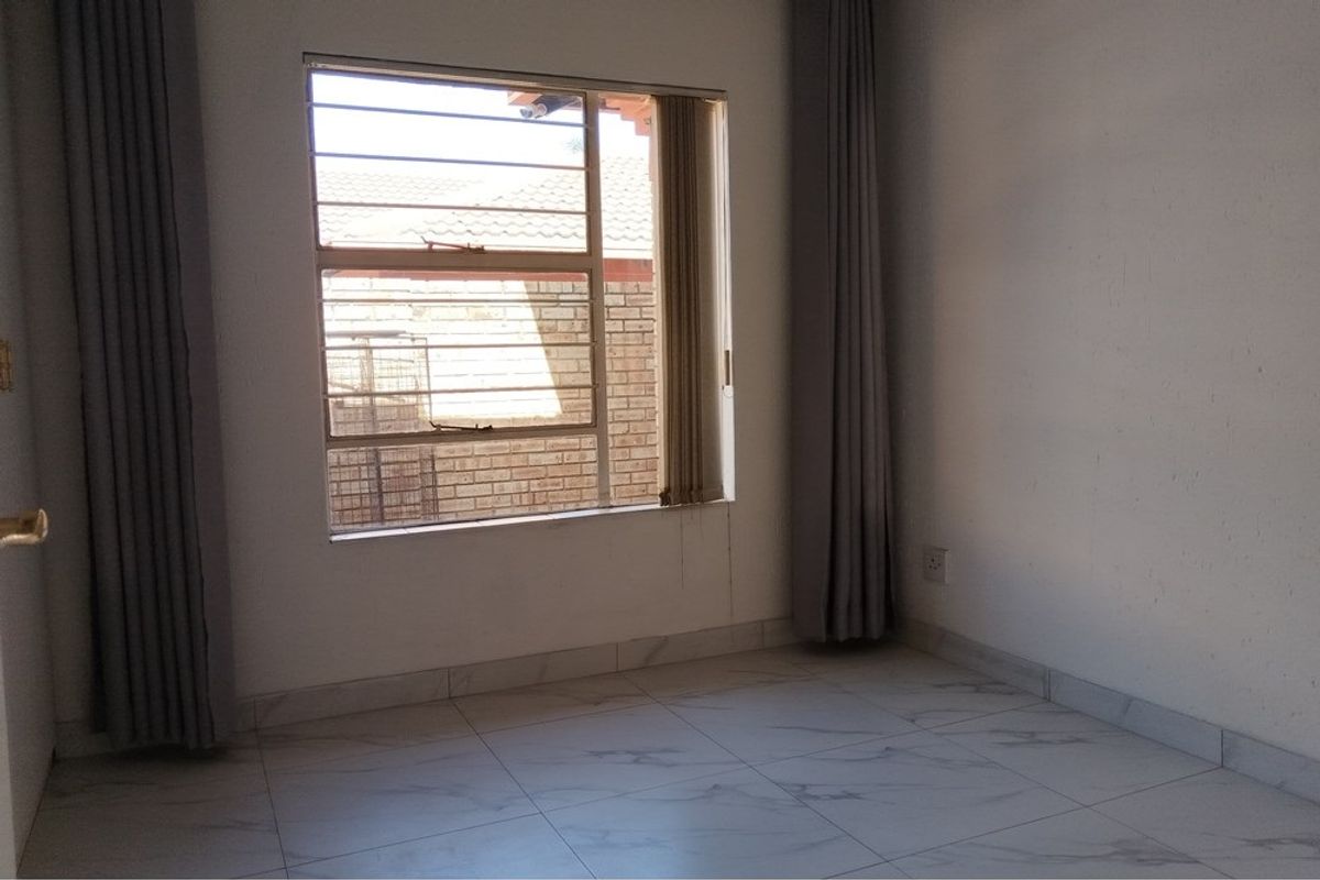 A bright, empty bedroom featuring modern tiled flooring and a window fitted with security bars.