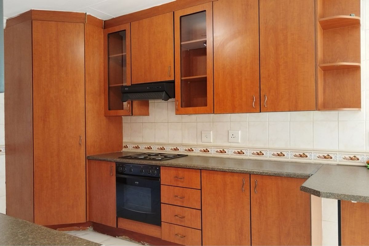 A functional kitchen featuring wood-look laminate cabinetry, built-in oven, hob, extractor fan, and tiled backsplash with a neutral countertop.