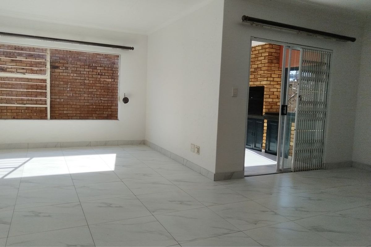 A bright, empty living area featuring modern marble-look floor tiles and a sliding glass door providing access to an outdoor patio space.