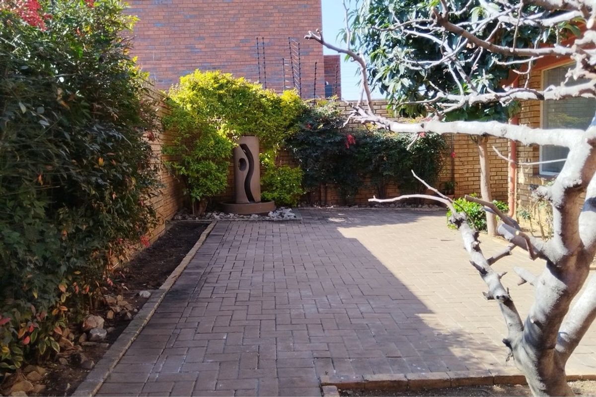 A private rear courtyard featuring brick paving, established garden borders, a decorative water feature, and secure brick boundary walls with electric fencing.