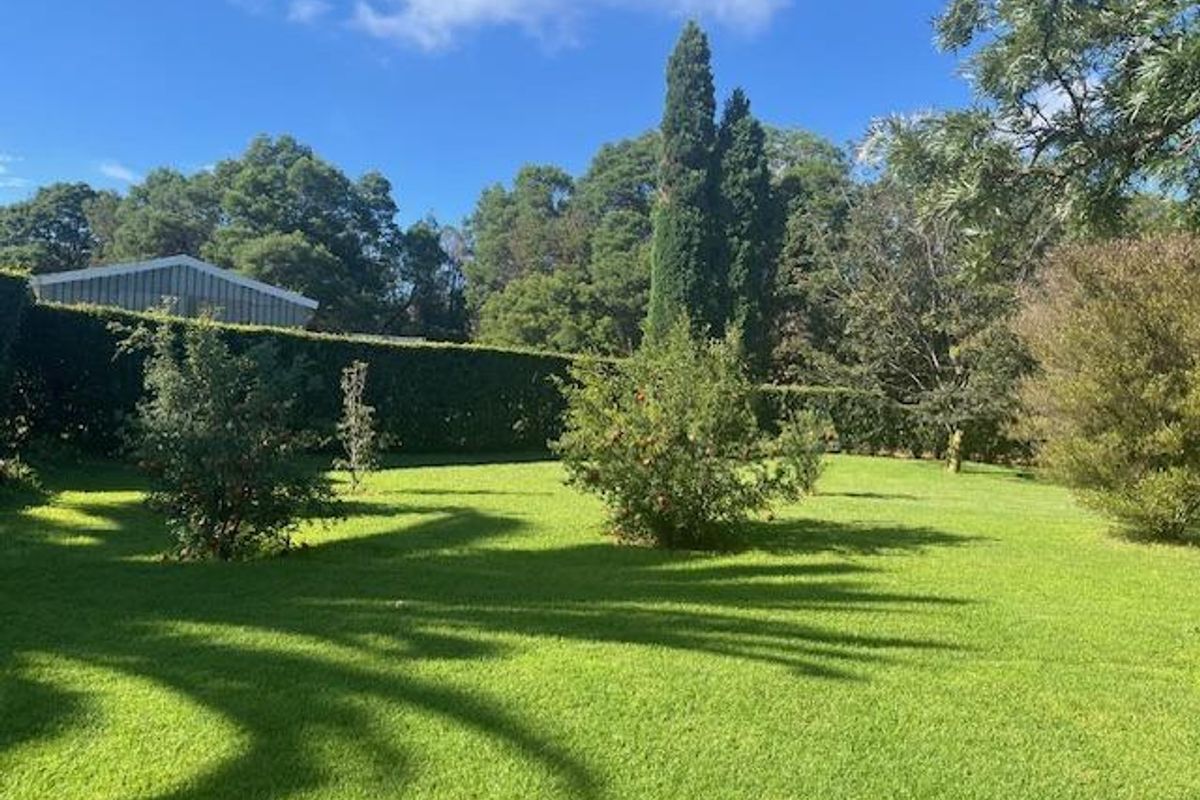 A well-maintained, expansive green lawn surrounded by mature trees and a manicured hedge, providing a private and serene outdoor setting.