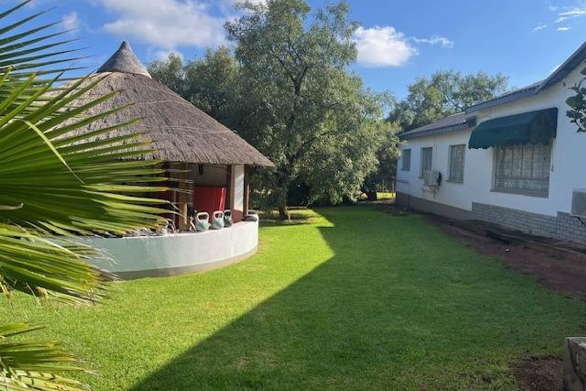 A view of the rear garden featuring a traditional thatched lapa structure and the side elevation of the main farmhouse building.