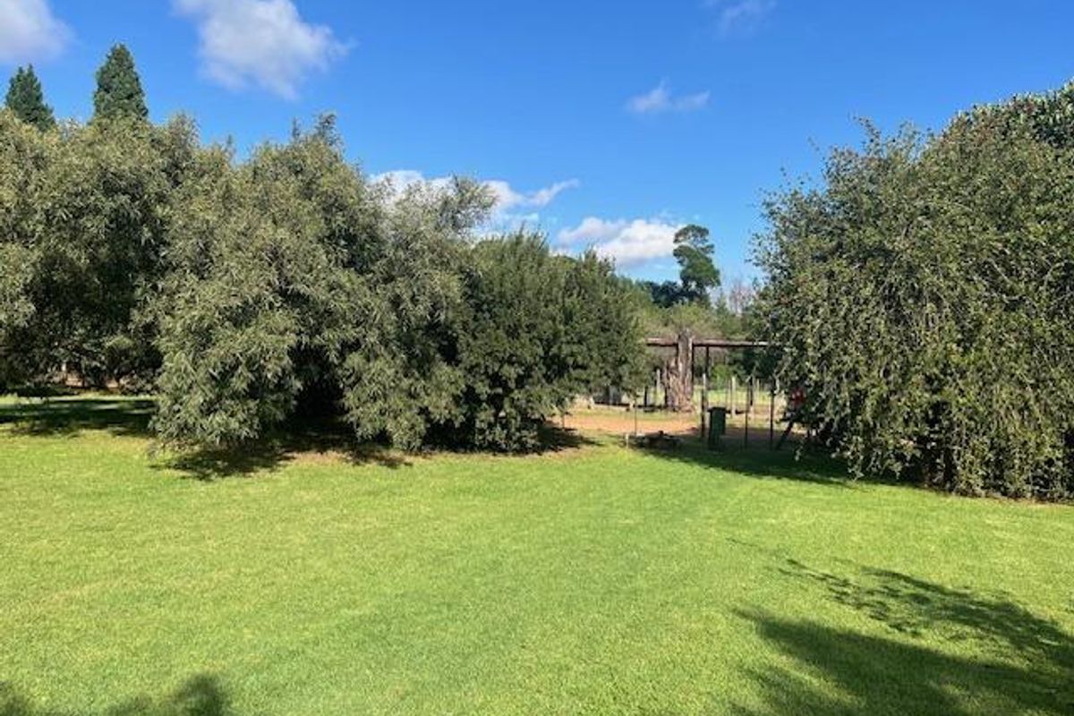 A well-maintained green lawn area on the farm property, featuring mature trees and established landscaping under a clear blue sky.