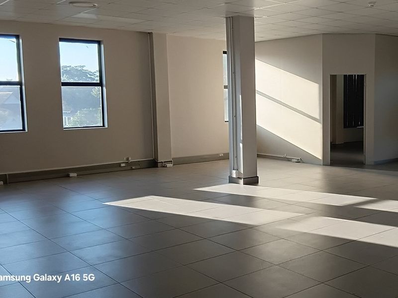 A spacious, open-plan office area featuring large windows, tiled flooring, and a central structural column, offering a bright and versatile workspace.