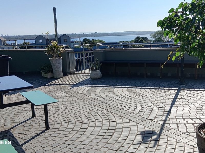 Spacious rooftop terrace featuring paved flooring, metal railings, and panoramic water views, ideal for outdoor office breaks or social gatherings.
