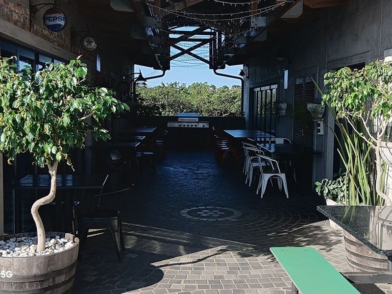 A covered outdoor patio area featuring paved flooring, exposed brickwork, and a built-in barbecue station, ideal for social gatherings or office break-out space.