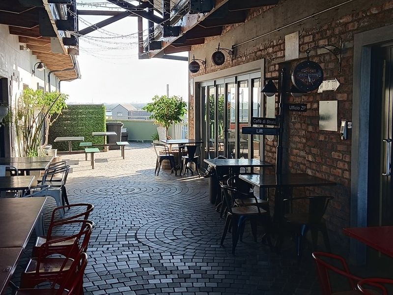 A spacious outdoor terrace area featuring exposed brick walls, paved flooring, and a covered structure, ideal for office break-out space or social gatherings.