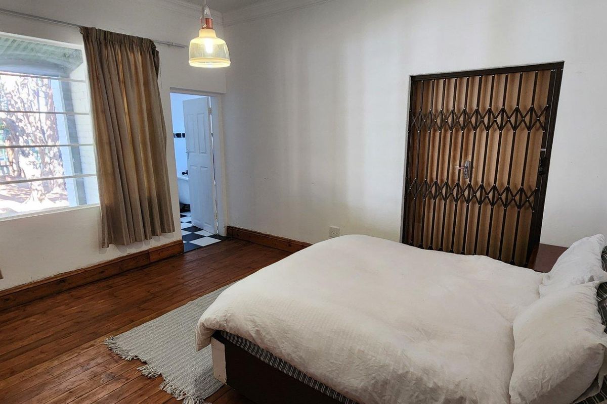 A bedroom featuring original hardwood flooring, a security gate, and direct access to an adjoining bathroom.
