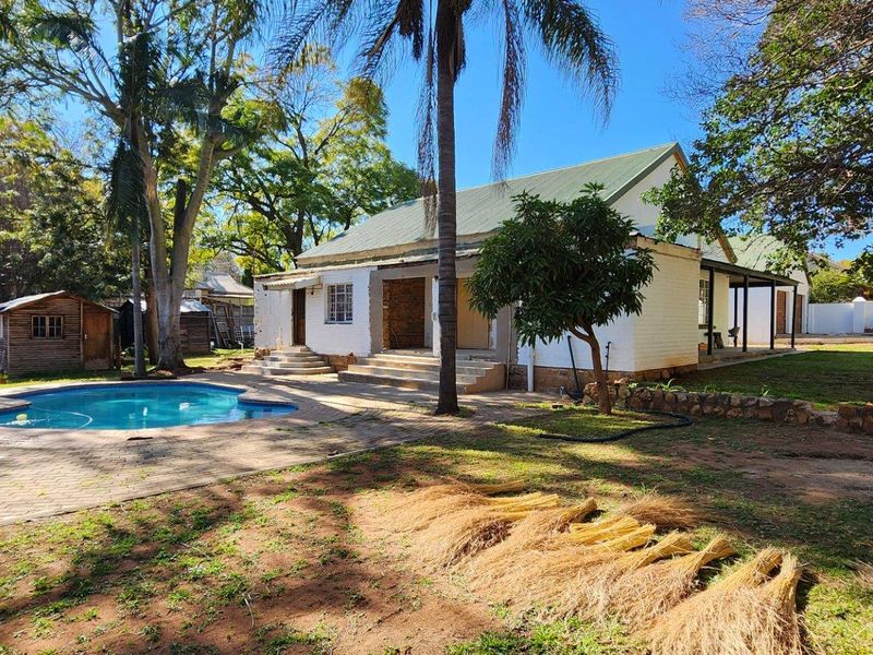 Rear view of the property featuring a swimming pool, paved patio area, and a spacious garden with mature trees and an outbuilding.