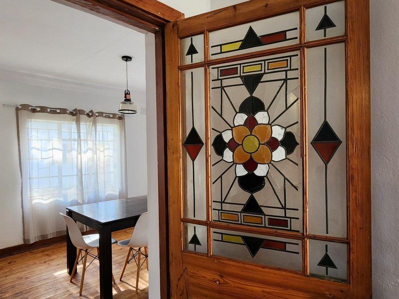 A view through a decorative stained glass timber door into a bright living area featuring polished wooden floors.