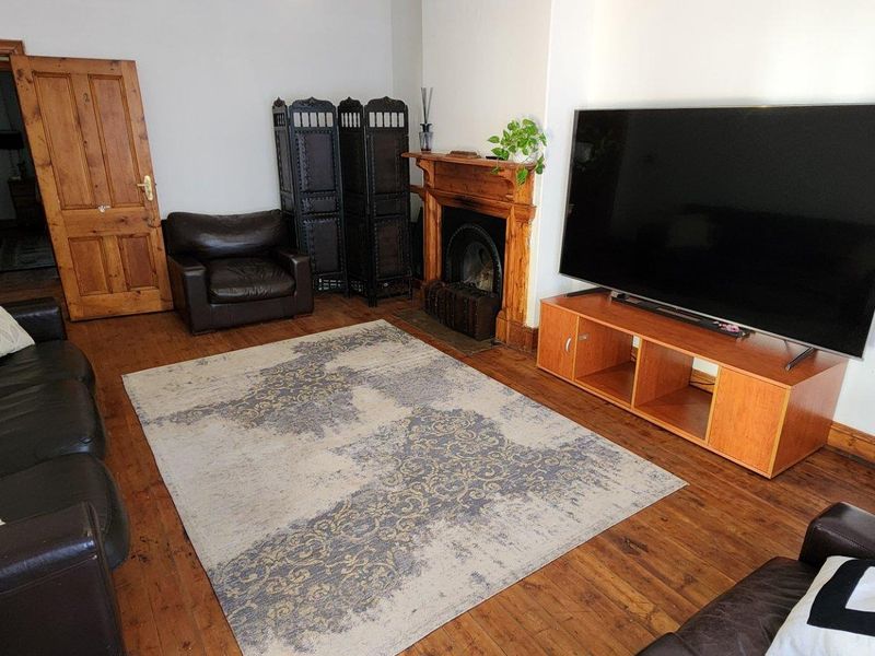 A living room featuring original wooden flooring, a traditional fireplace with a wooden mantel, and classic wooden door frames.
