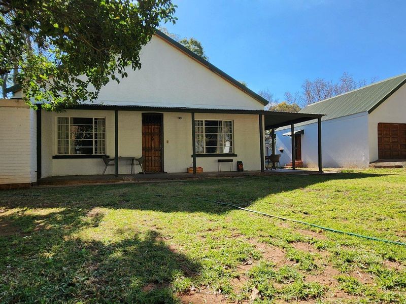 Rear view of the house featuring a covered patio, established garden, and a detached garage with timber doors.