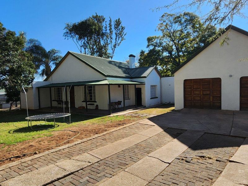 Rear view of the property featuring a covered patio, a double garage with wooden doors, and a spacious garden area with a paved driveway.