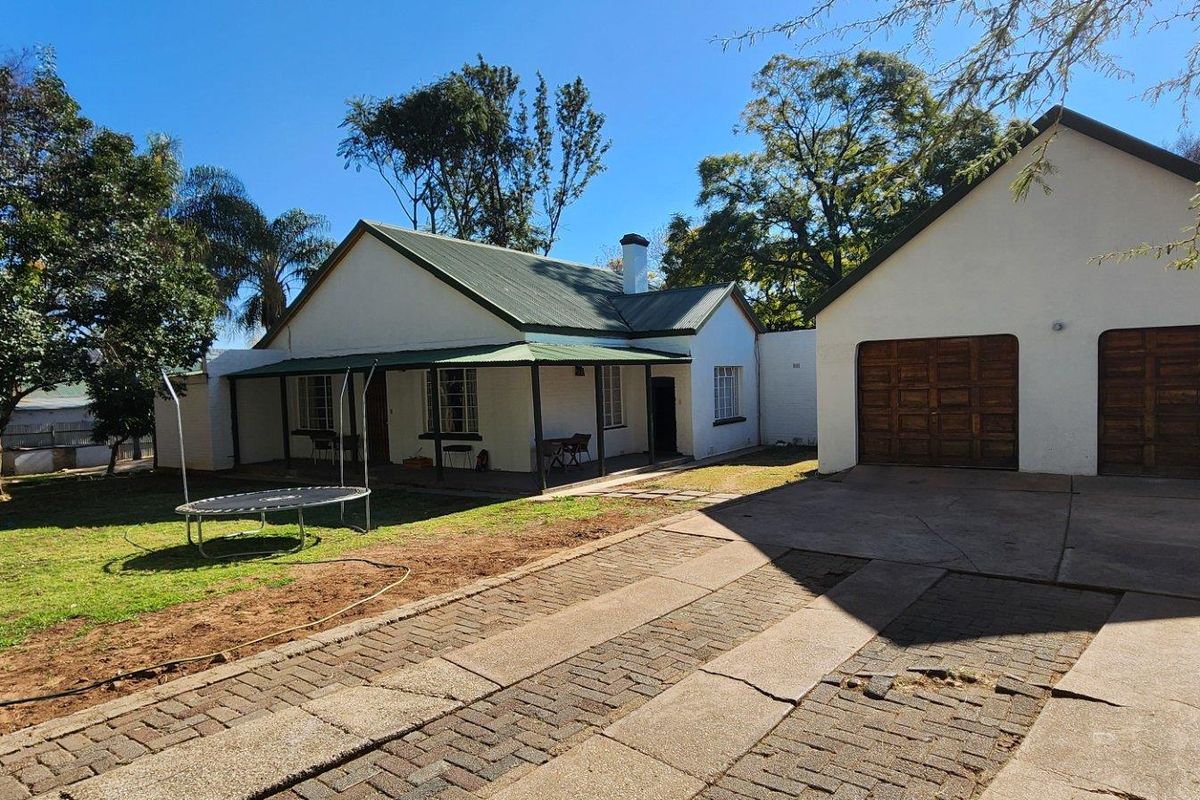 Rear view of the property featuring a covered patio, a double garage with wooden doors, and a spacious garden area with a paved driveway.