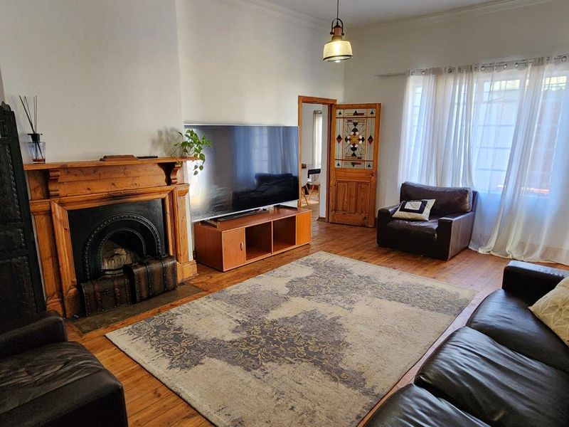 A living room featuring timber flooring, a classic fireplace with a timber mantel, and a decorative stained glass door.