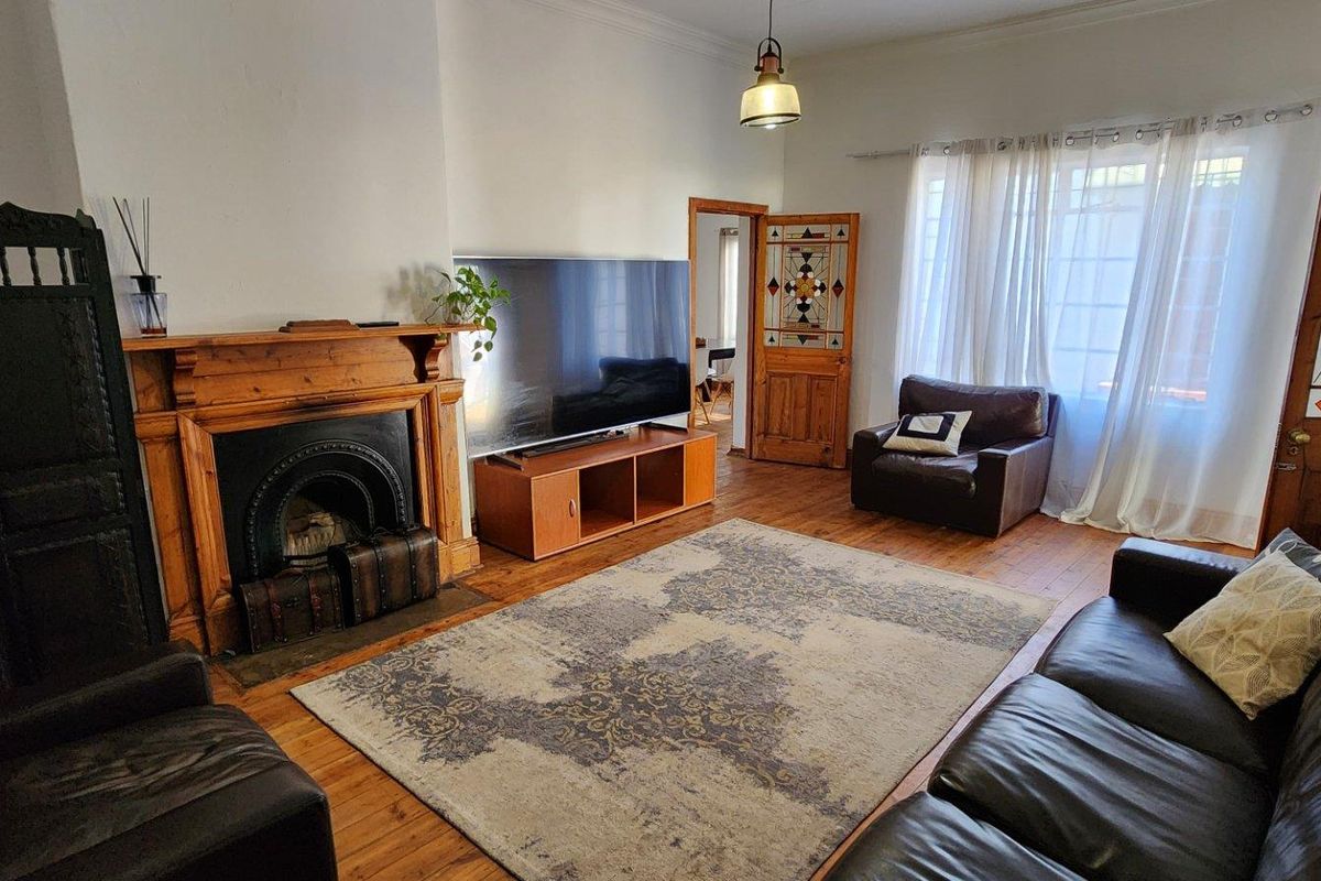 A living room featuring timber flooring, a classic fireplace with a timber mantel, and a decorative stained glass door.