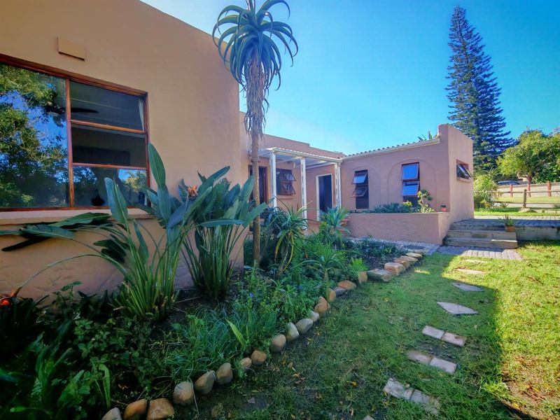 Rear exterior view of the house featuring a landscaped garden, stone-edged pathways, and a covered patio area with timber-framed windows.
