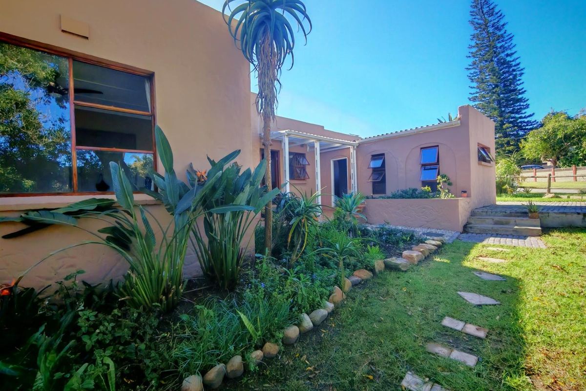 Rear exterior view of the house featuring a landscaped garden, stone-edged pathways, and a covered patio area with timber-framed windows.