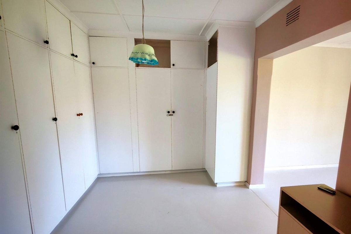 A bedroom featuring extensive built-in white cupboards and a neutral floor, offering a blank canvas for potential renovation and interior design updates.