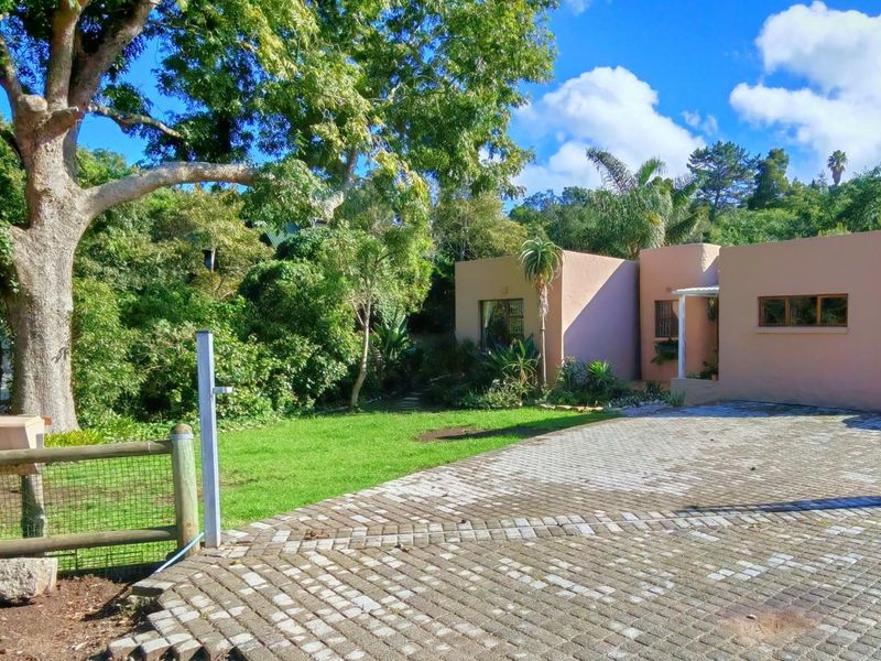 Front view of the property featuring a paved driveway, established garden with mature trees, and a secure fenced entrance.