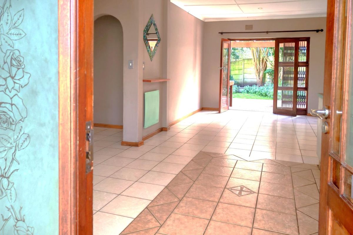 Spacious, light-filled living area featuring neutral tiled flooring, an elegant archway, and double doors providing seamless access to the rear garden.