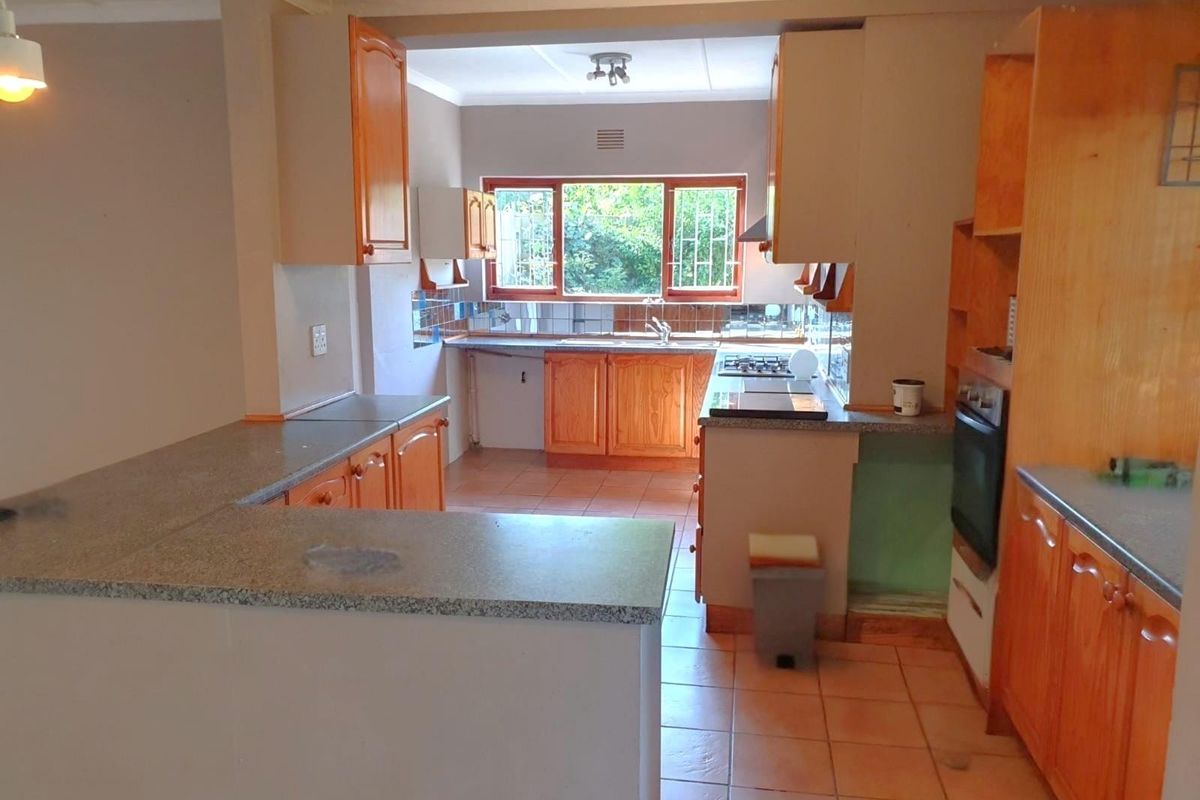A functional kitchen featuring wooden cabinetry, granite countertops, built-in oven, and gas hob, with tiled flooring and natural light from the rear window.