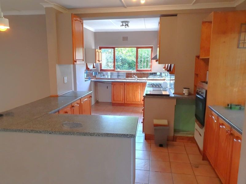 A functional kitchen featuring wooden cabinetry, granite countertops, built-in oven, and gas hob, with tiled flooring and natural light from the rear window.