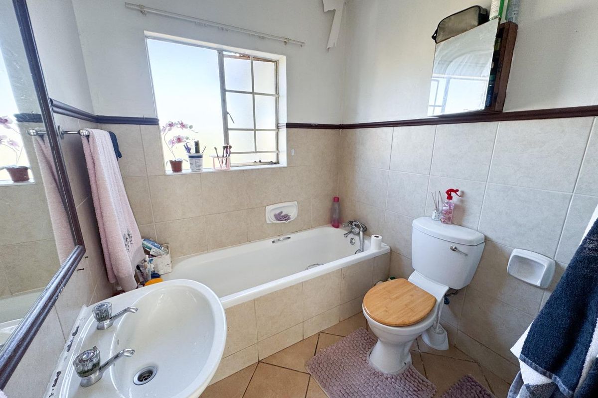 A functional bathroom featuring a bathtub, pedestal basin, and toilet with tiled walls and flooring, requiring some cosmetic maintenance to the ceiling.