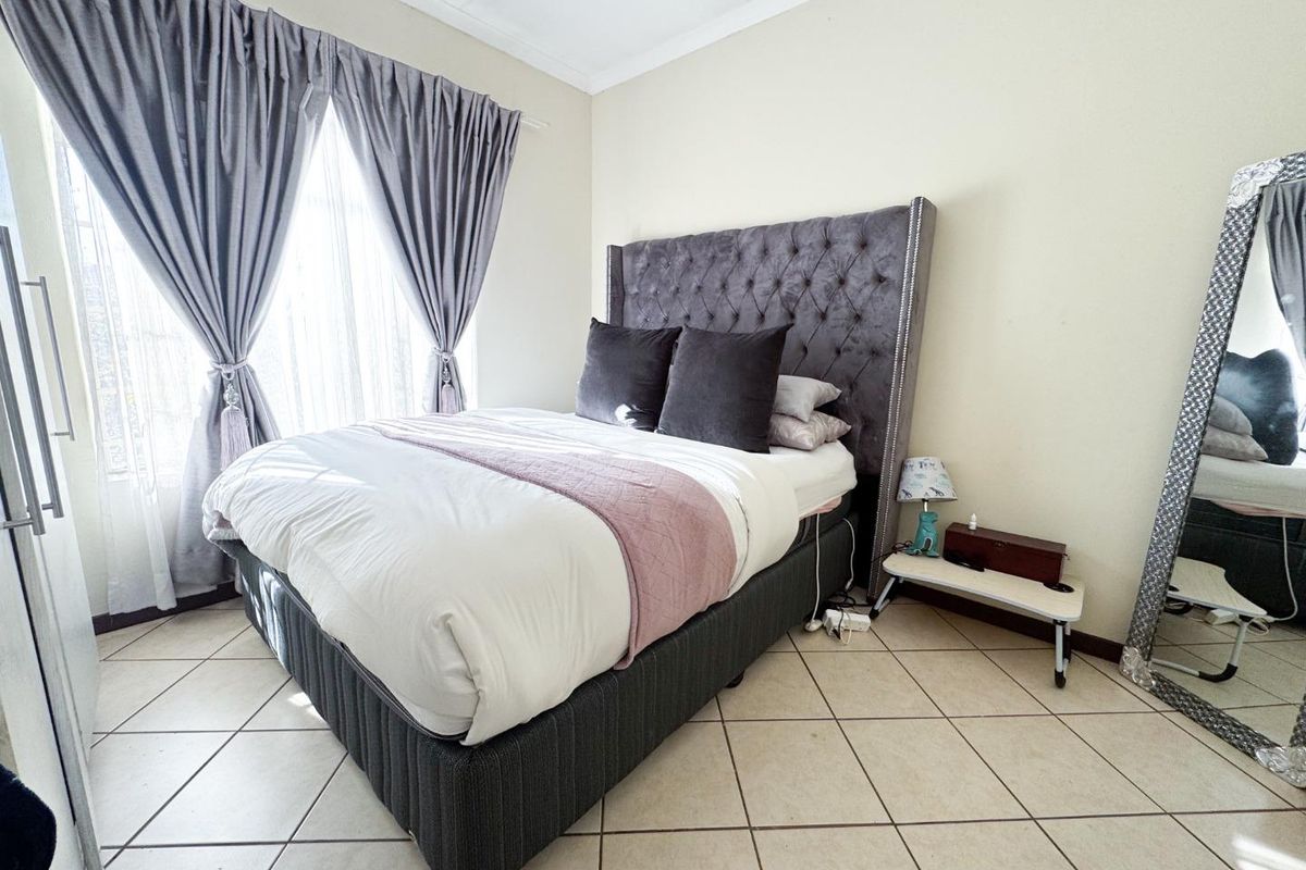 A bedroom featuring tiled flooring and a large window with curtain treatments.
