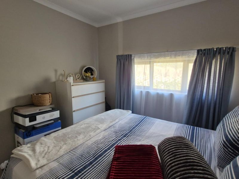 A standard bedroom featuring neutral wall tones and a window with installed curtain tracks, providing natural light to the space.