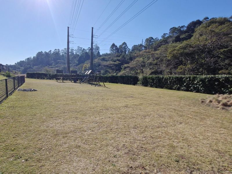 A spacious, open garden area featuring a lawn, perimeter wire fencing, and established hedging, with a small playground structure in the background.