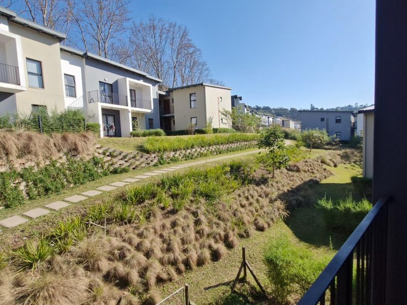 A view from a balcony overlooking a landscaped communal garden area with terraced retaining walls and paved pathways between townhouse units.