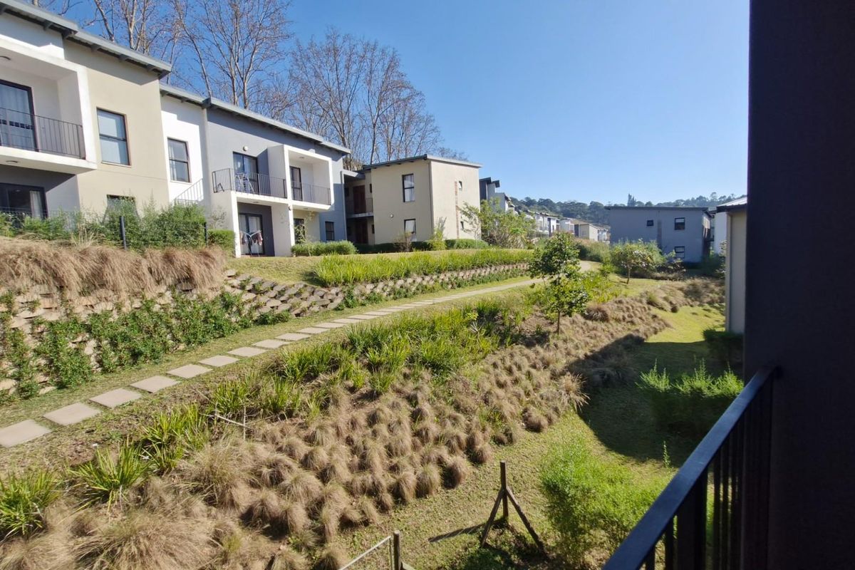 A view from a balcony overlooking a landscaped communal garden area with terraced retaining walls and paved pathways between townhouse units.