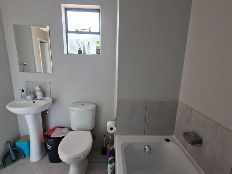 A functional bathroom featuring a pedestal basin, toilet, and bathtub with tiled splashback, providing essential amenities in a compact layout.