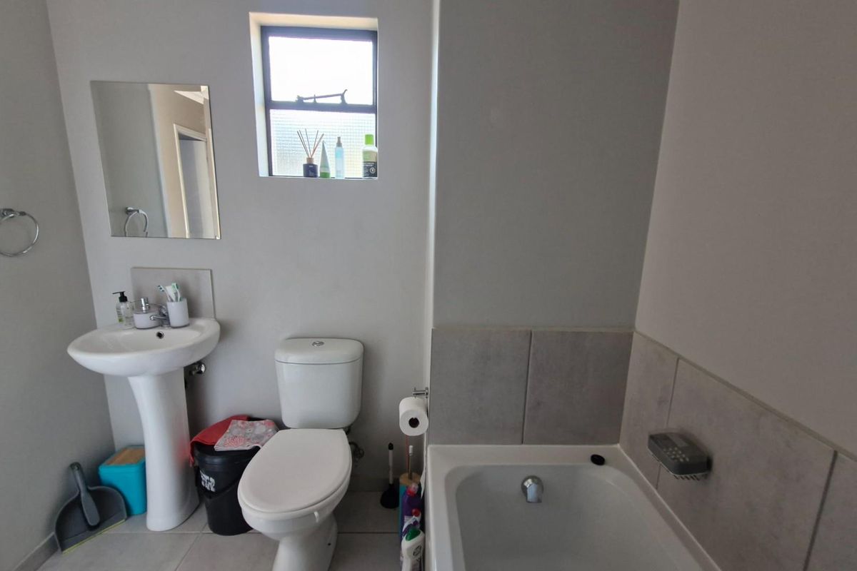 A functional bathroom featuring a pedestal basin, toilet, and bathtub with tiled splashback, providing essential amenities in a compact layout.