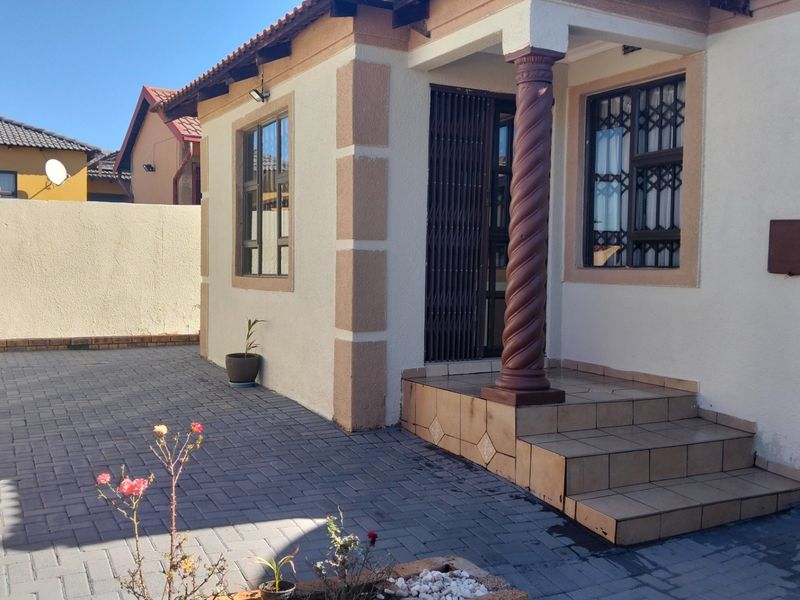 Front entrance of the house featuring tiled steps, a decorative spiral column, security gate, and a paved driveway area.
