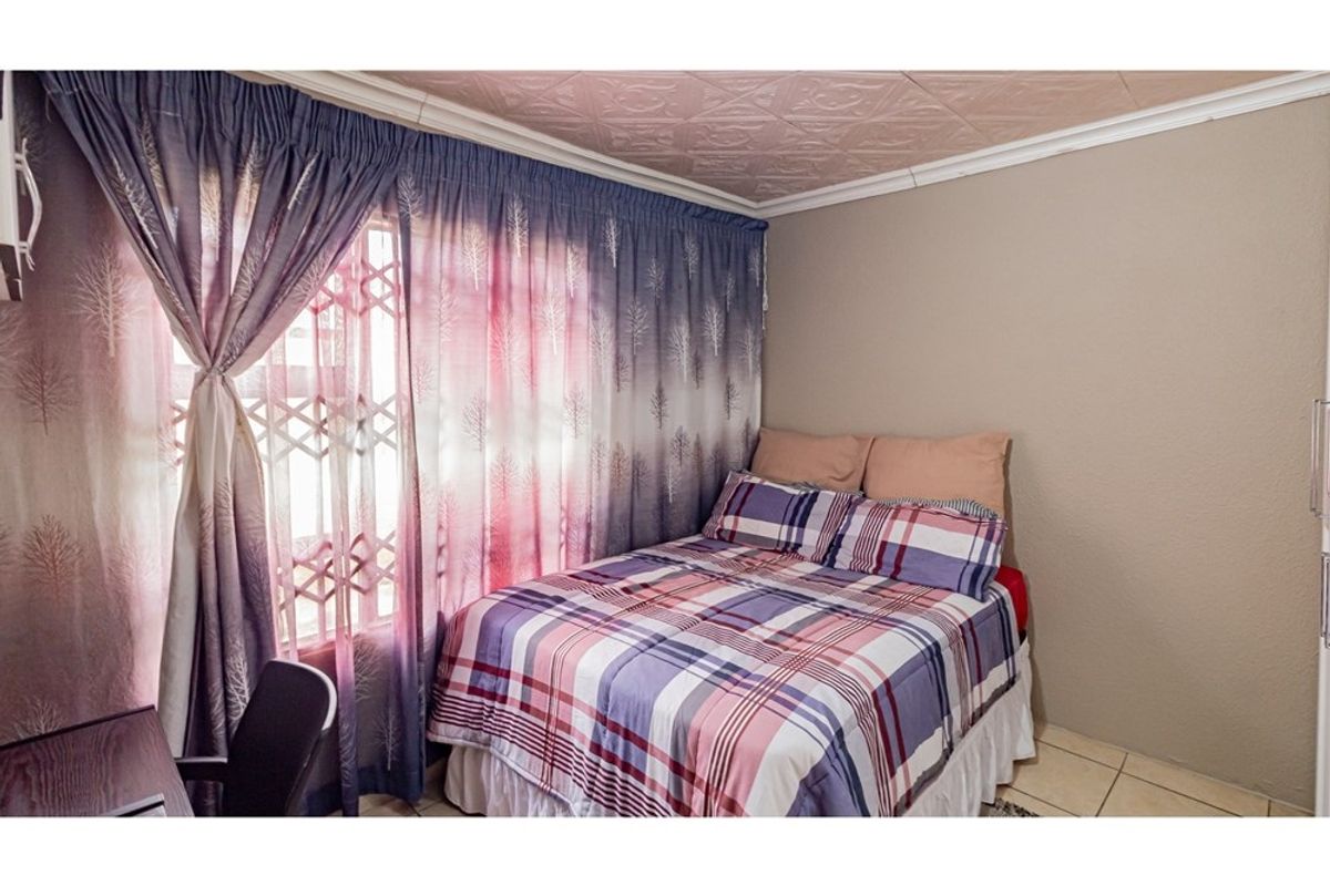 A bedroom featuring tiled flooring, a textured ceiling, and a security gate on the window.