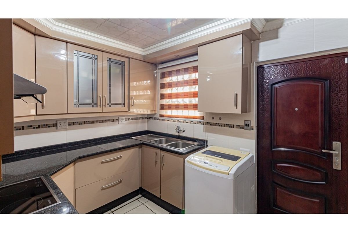 Compact kitchen featuring high-gloss cabinetry, granite countertops, a double-basin stainless steel sink, and integrated laundry plumbing.