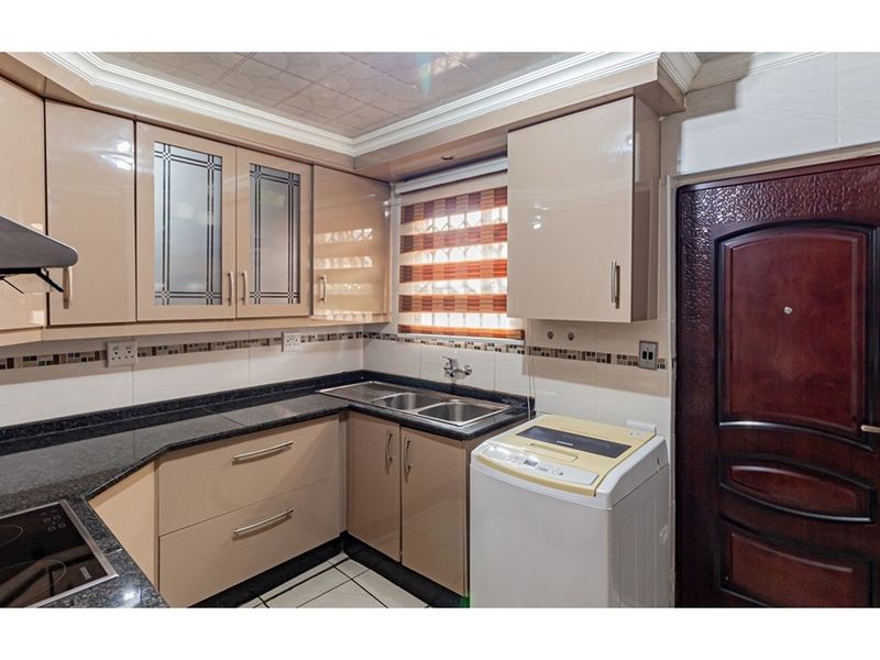 Compact kitchen featuring high-gloss cabinetry, granite countertops, a double-basin stainless steel sink, and integrated laundry plumbing.
