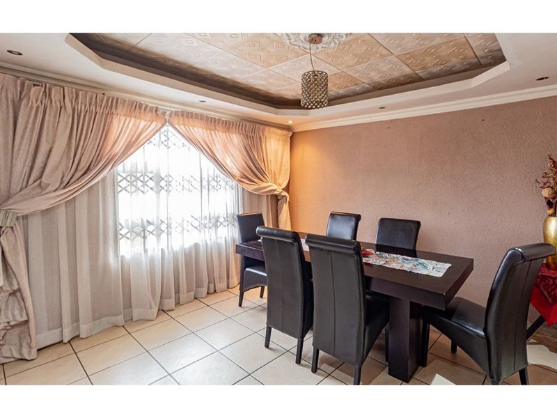 A dining room featuring tiled flooring, a decorative coffered ceiling with recessed lighting, and a large window with security bars.