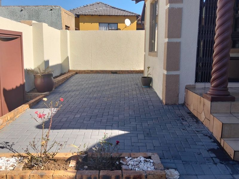 A neat paved rear courtyard featuring brick planter boxes, tiled entrance steps with a decorative pillar, and secure boundary walls.