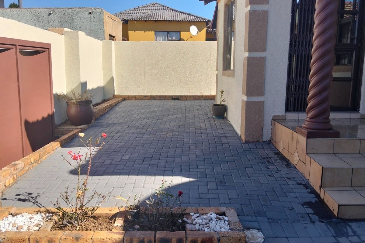 A neat paved rear courtyard featuring brick planter boxes, tiled entrance steps with a decorative pillar, and secure boundary walls.