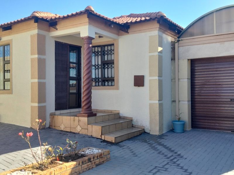 Front elevation of a single-story home featuring a tiled entrance with a decorative pillar, paved driveway, and an integrated garage with a roller door.