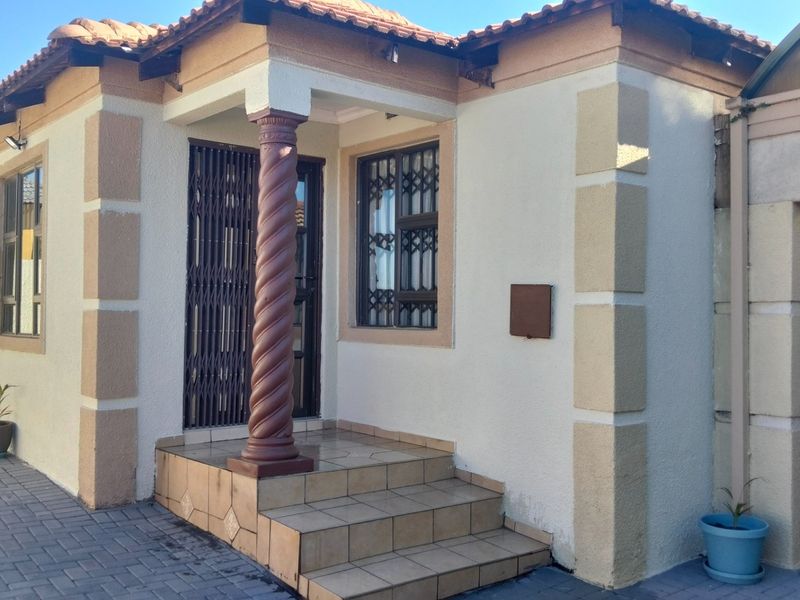 Front entrance of the house featuring tiled steps, a decorative column, security gate, and paved driveway access.