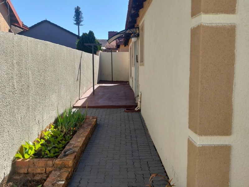 A side exterior pathway featuring a paved walkway, a brick planter box, and a concrete patio area along the side of the house.