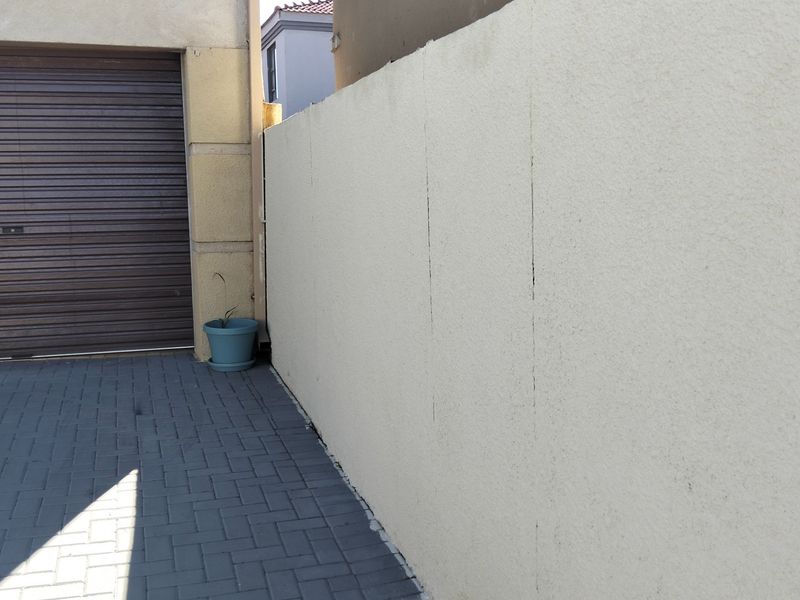 A view of the property's paved driveway, roller garage door, and a boundary wall showing visible vertical cracking.