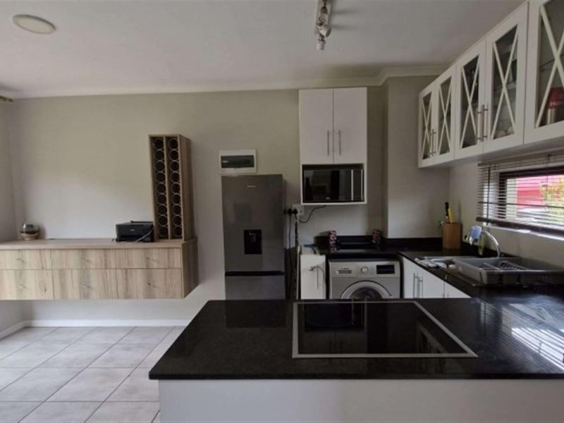 Modern kitchen featuring dark granite countertops, built-in cabinetry, integrated appliances, and tiled flooring with direct access to the outdoor area.